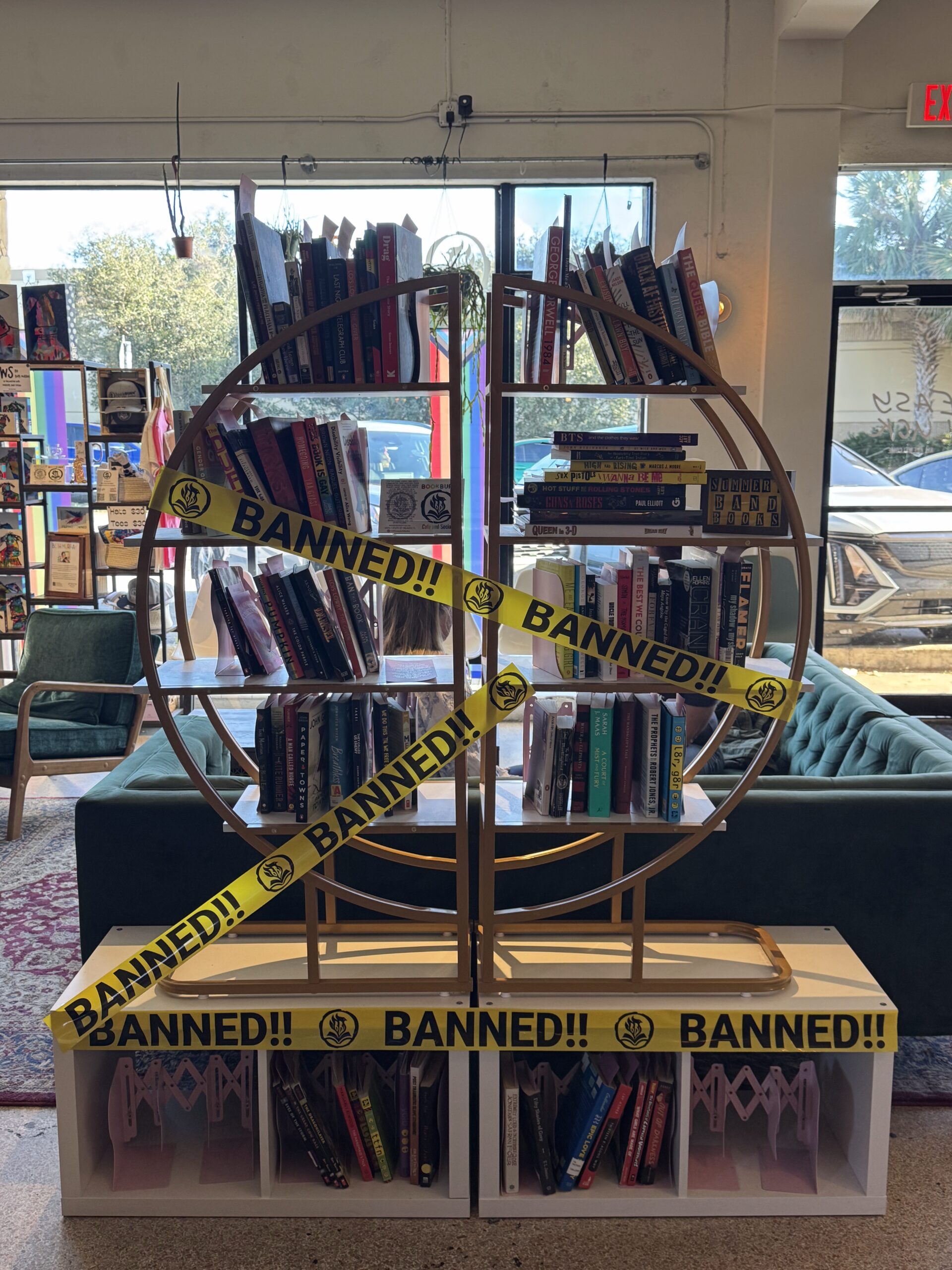 Circular bookshelf wrapped in yellow “BANNED” tape displaying banned books at BookBurn Café and Social in Orlando.