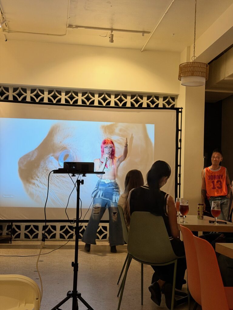 Live performer hosting an LGBTQIA+ entertainment event inside BookBurn Cafe and Social in Orlando’s Milk District while guests watch from café tables.