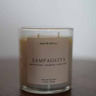 Slow and Still Co. Sampaguita soy wax candle in a glass jar displayed on a table at BookBurn Cafe and Social