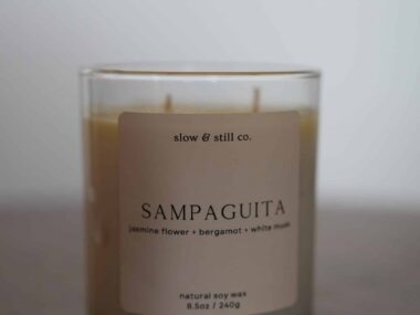 Slow and Still Co. Sampaguita soy wax candle in a glass jar displayed on a table at BookBurn Cafe and Social