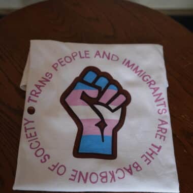 T-shirt with trans pride fist design and message about trans people and immigrants displayed in Orlando