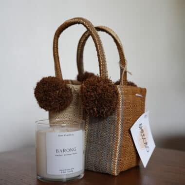 Handwoven mini tote bag with pom pom accents next to soy candle at BookBurn Cafe in Orlando
