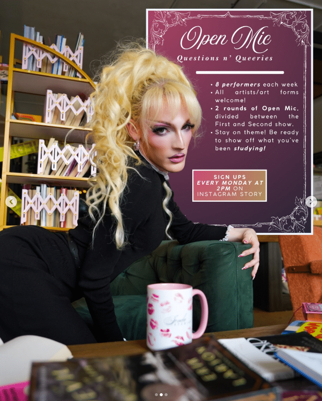 Drag Queen posing inside BookBurn Cafe and Social beside a promotional sign for Jenda Studies Open Mic, a queer-friendly drag open mic event welcoming all artists and art forms.